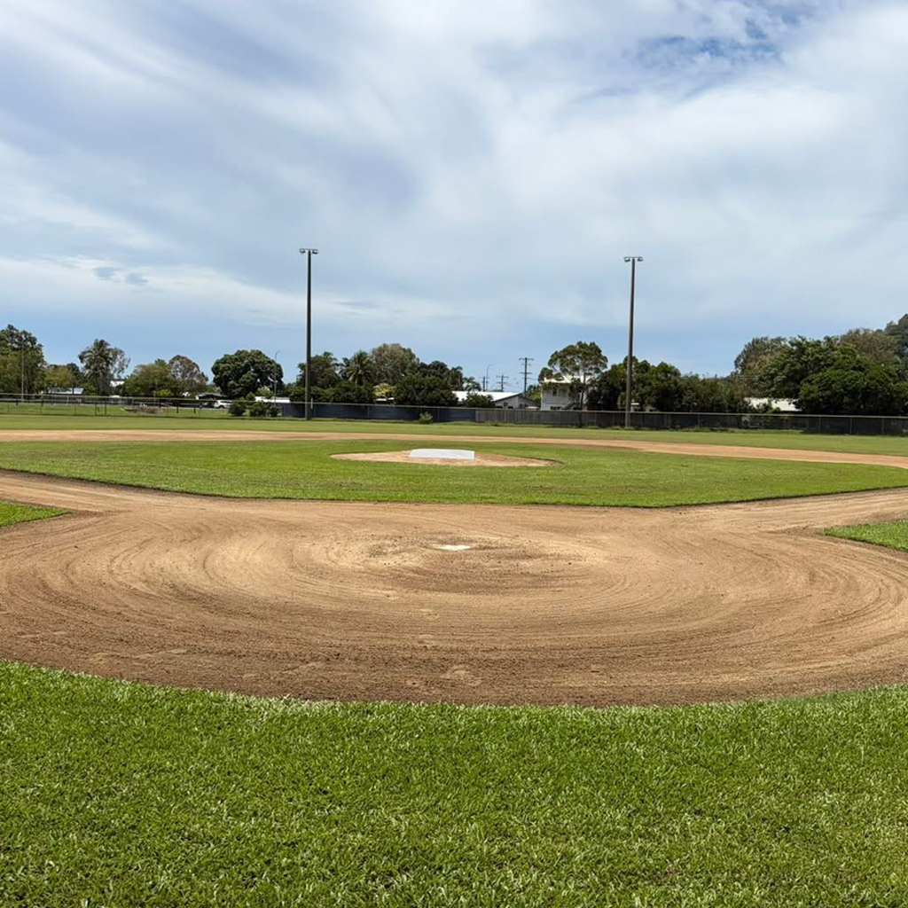 Baseball field with dirt infield and pitcher's mound under a blue sky.
